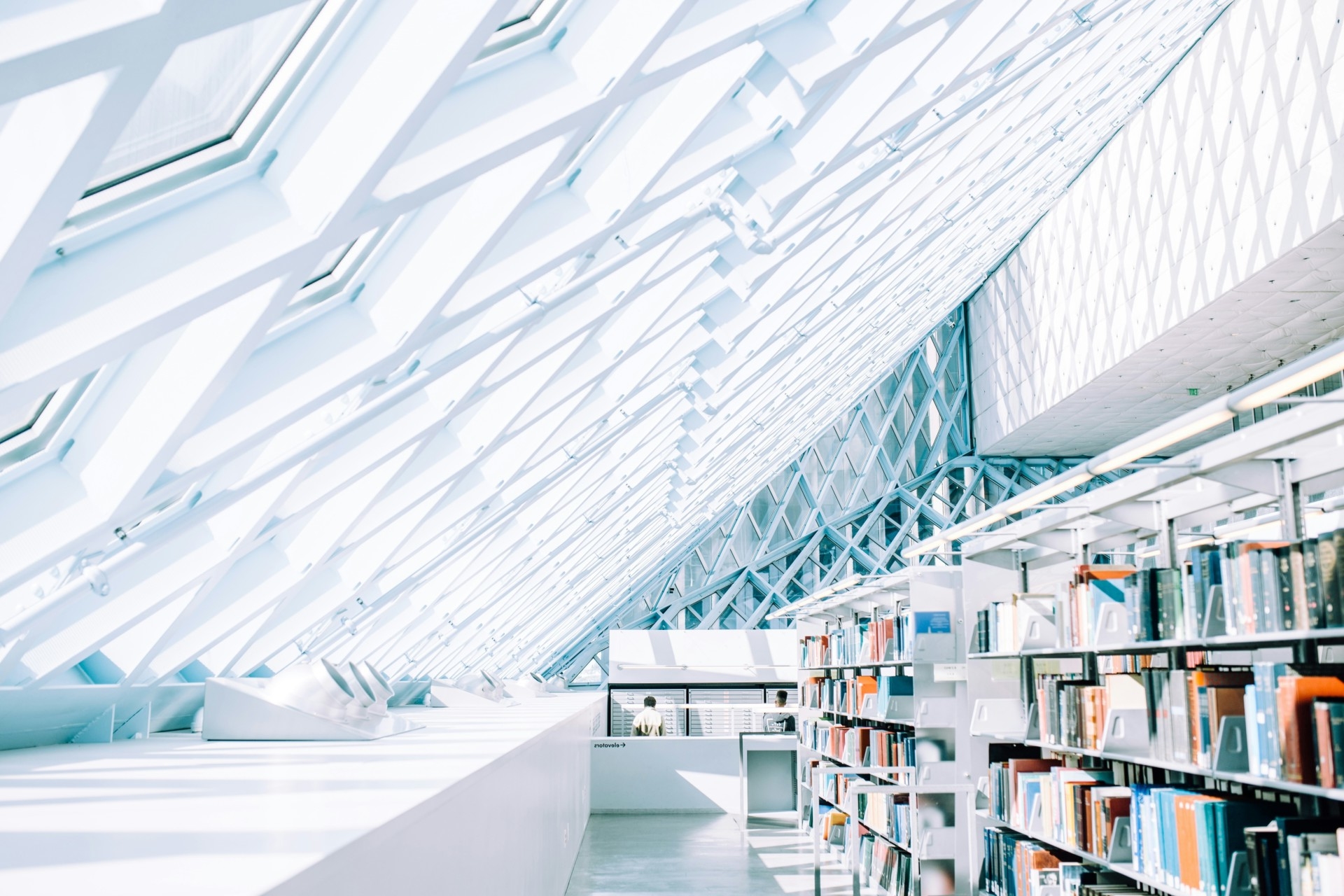 Image d'une bibliothèque moderne avec des étagères remplies de livres, sous un plafond en verre créant des motifs de lumi
