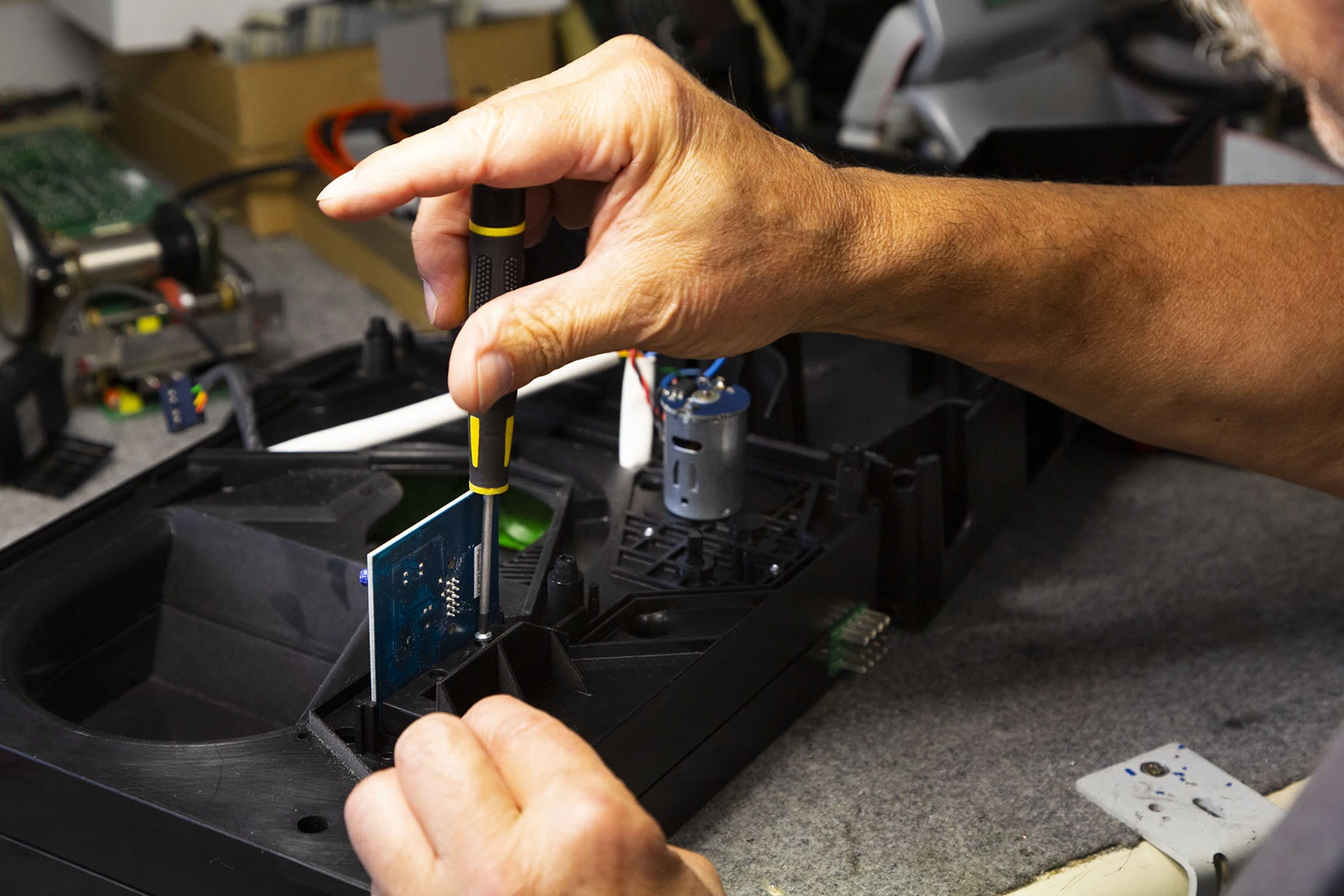 L'image montre une personne utilisant un tournevis pour travailler sur un composant électronique sur une table de travail.
