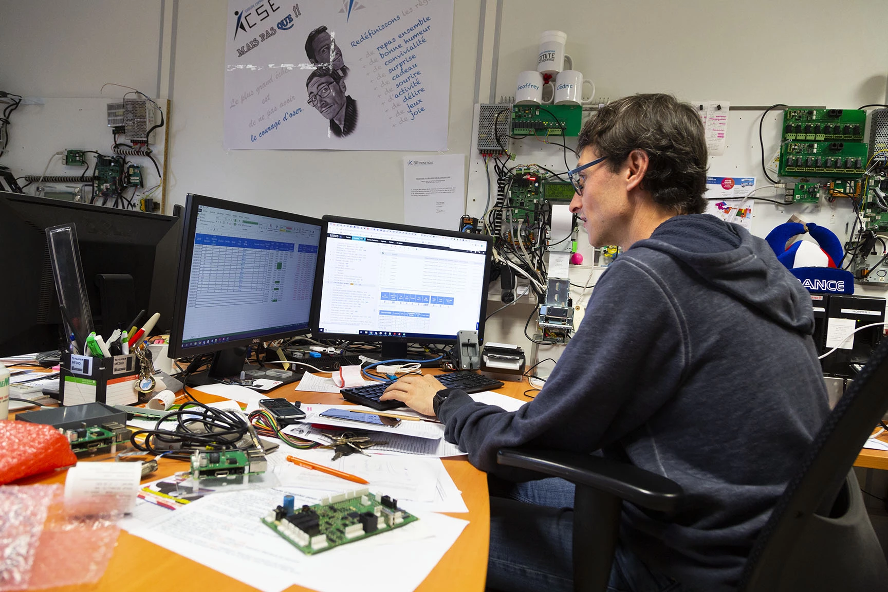 Un individu travaille sur un ordinateur dans un espace de travail encombré avec des composants électroniques et des moniteu