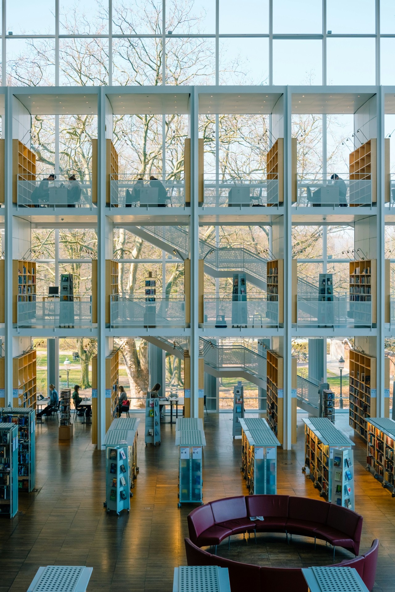 Cette image montre l'intérieur d'une bibliothèque moderne avec de grandes fenêtres, des étagères de livres et des espace