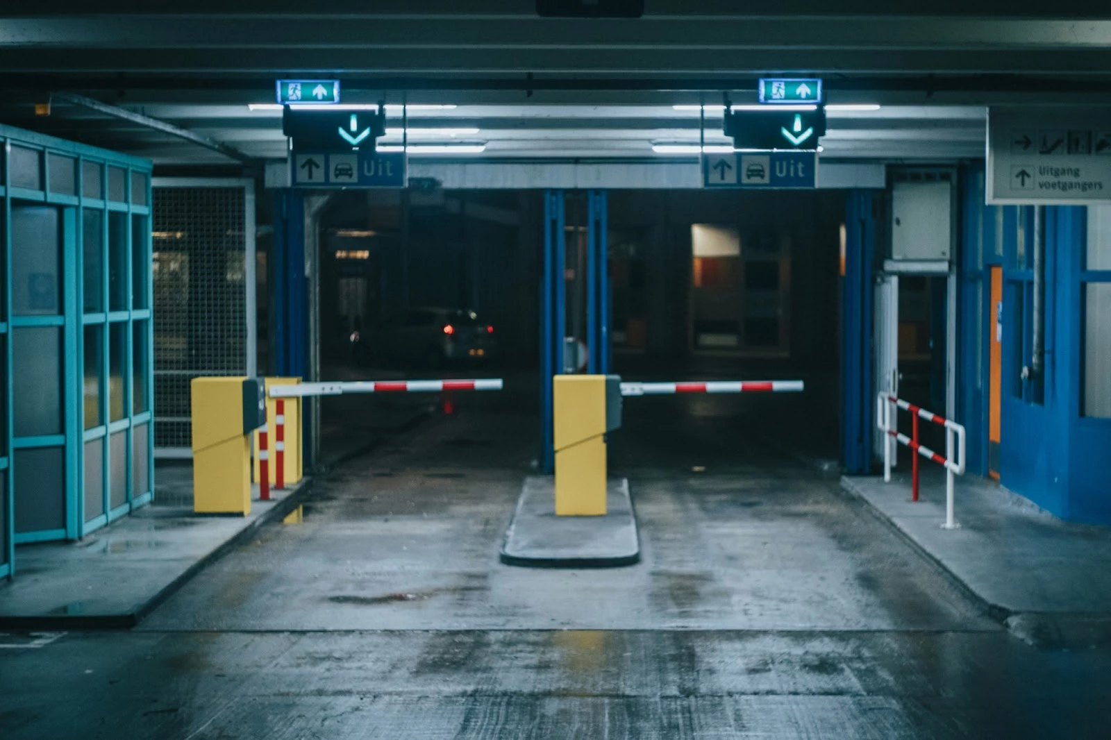 L'image montre une entrée de parking avec des barrières abaissées et des panneaux indiquant les sorties et les ascenseurs.