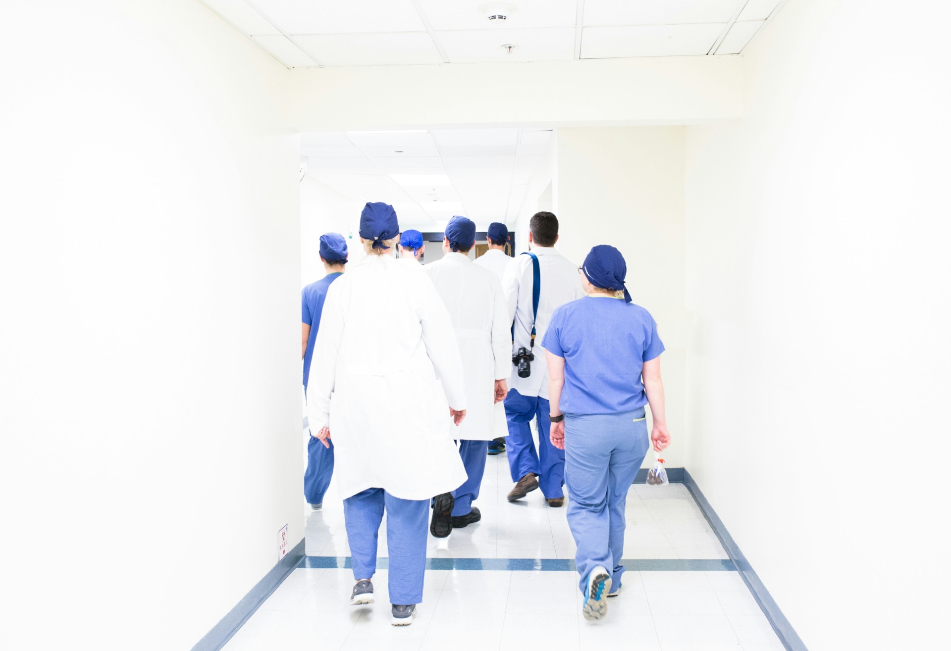Un groupe de professionnels de santé, vêtus de blouses blanches et de tenues bleues, marche dans un couloir d'hôpital.