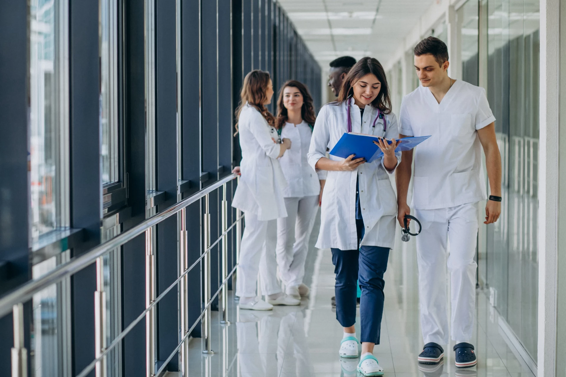 Quatre professionnels de santé, en blouses blanches, marchent dans un couloir moderne. Une femme tient des dossiers médicau